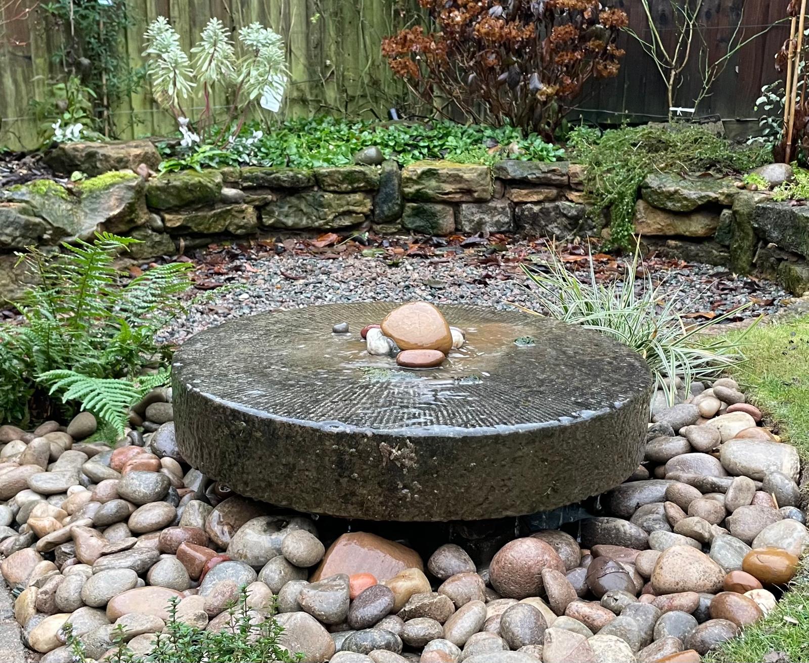 Millstone water feature with natural stone wall