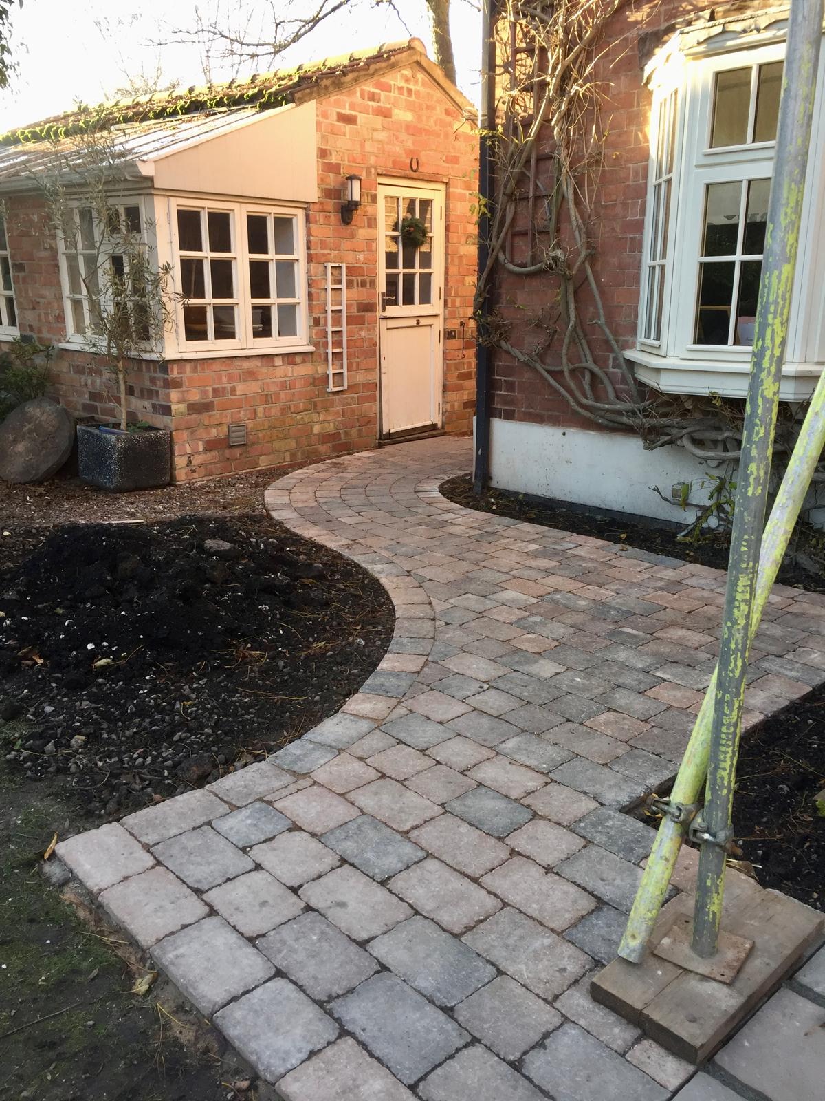 Curved tumbled block paving path to cottage-style property