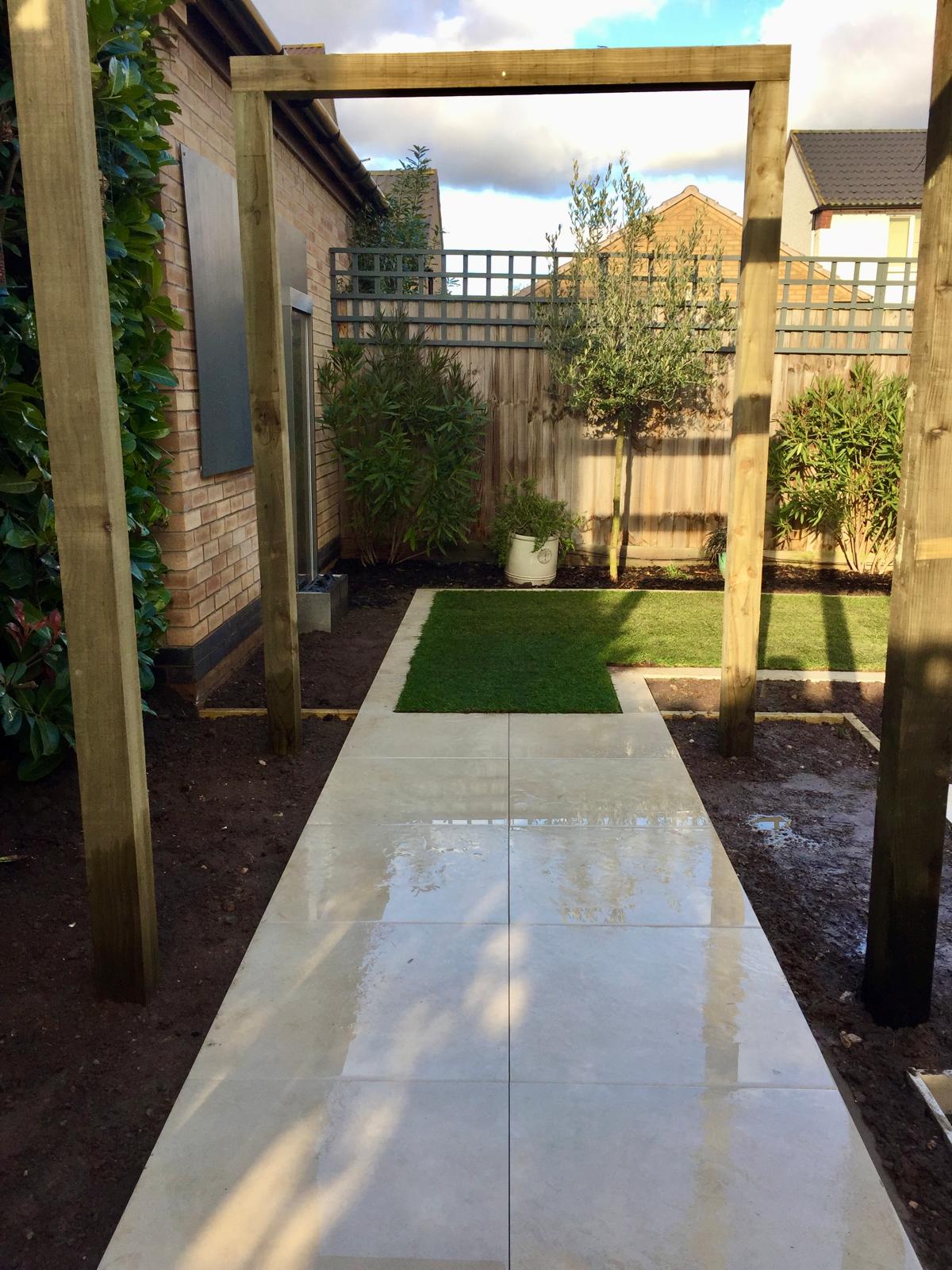 Contemporary porcelain paving garden with pergola and olive tree